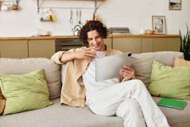 Zarif bir iş elbisesi içinde şık bir genç adam rahat bir evde tablet kullanırken gülümsüyor..