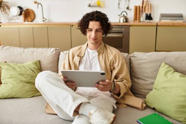 Modern iş kıyafetleri içinde genç bir adam bir tabletle meşgul, rahat bir ev atmosferi sergiliyor..
