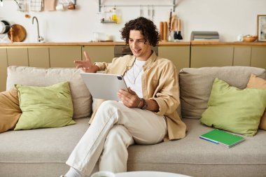 İş kıyafeti giymiş yakışıklı genç bir adam rahatça otururken tabletle etkileşime geçiyor..