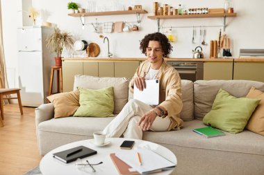 Modern bir yaşam alanında dizüstü bilgisayarla çalışırken şık giyinen yakışıklı genç adam gülümsüyor..