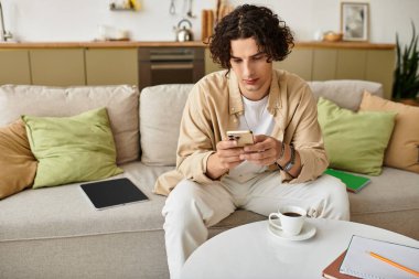 İş elbiseli genç adam rahatça oturur, akıllı telefonuna ve kahvesine odaklanır..