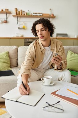 Yakışıklı bir genç adam telefonuna not alırken kahveden zevk alır..