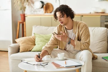 Yakışıklı genç adam lüks bir yaşam alanında not defteri ve telefonla yaratıcı düşüncelere dalmış.