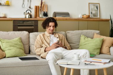 Akıllı iş kıyafetleri giymiş genç bir adam rahat bir koltukta rahatlar ve telefonunun tadını çıkarır..