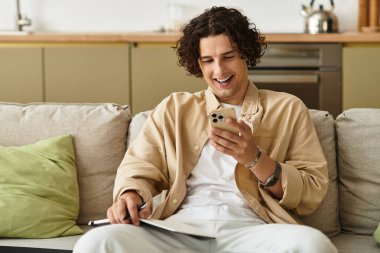 Şık bir genç adam rahat bir koltukta oturup telefonuna gülümsüyor ve boş zamanlarının tadını çıkarıyor..