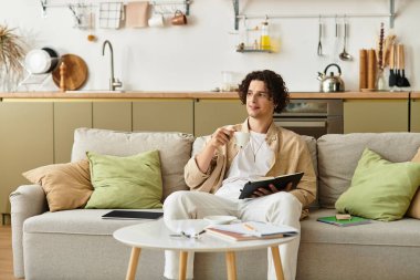 İş kıyafetli yakışıklı genç adam düşünceli bir ifadeyle koltukta rahatça oturur..