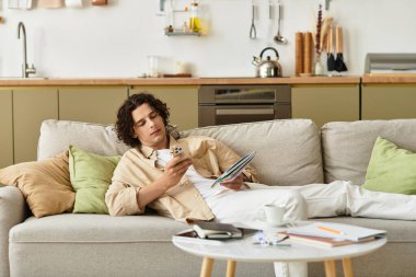 Genç adam, modern hayattaki akıllı telefonu ve tabletine odaklanmış bir şekilde kanepede dinleniyor..