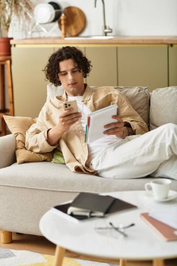 İş kıyafetleri içinde şık bir genç adam rahat bir yaşam alanında akıllı telefonuyla iletişim kuruyor..