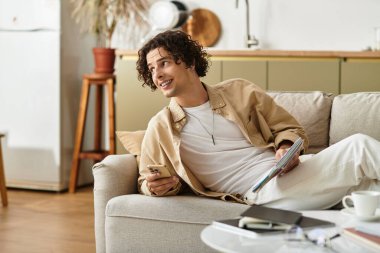 İş kıyafetleri içindeki yakışıklı genç adam bir kanepede rahatça oturup dergilerle meşgul oluyor..