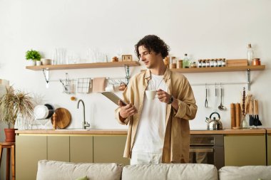 İş elbiseleri içindeki genç adam, modern bir mutfakta kahve ve notlarla rahatlıyor..