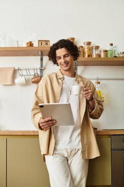 Sıradan iş kıyafetleri içindeki yakışıklı genç adam elinde bir kupayla tabletine bakarken gülümsüyor..