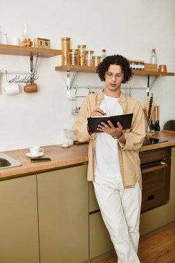 Yakışıklı genç adam şık bir mutfakta, tabletine odaklanmış duruyor..