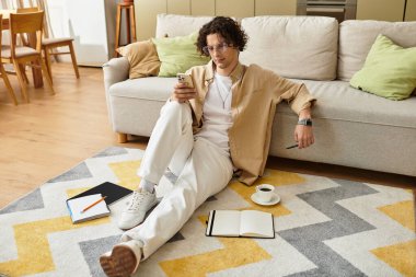 Şık bir iş elbisesi giymiş yakışıklı genç adam akıllı telefonunu kullanırken rahatça oturur..