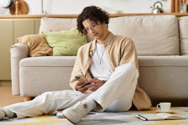 Yakışıklı adam iş kıyafetleriyle yerde oturup rahat bir yerde telefonunu okumaya odaklanmış..