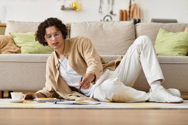 İş kıyafetleri içinde genç bir adam yerde rahatça otururken yaratıcı işlerde çalışıyor..