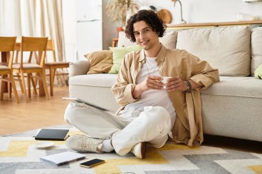 İş elbiseleri içindeki yakışıklı genç adam yerde rahatlıyor, içkisinin tadını çıkarıyor ve etrafı teknolojiyle çevrili..