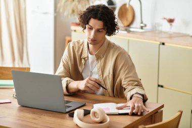 İş elbiselerindeki yakışıklı genç adam not yazarken özenle laptopunun başında çalışıyor..