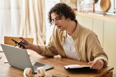 Yakışıklı bir genç adam şık bir ev ofisinde çalışırken akıllı telefonuna odaklanır..