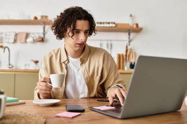 Şık bir iş elbisesi giymiş yakışıklı genç bir adam kahvesini yudumlarken dizüstü bilgisayarına odaklanıyor..