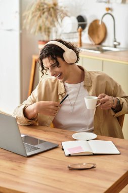 Şık giyinen genç adam evde çalışıyor, kulaklık takıp kahve içiyor..