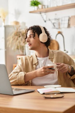 Yakışıklı genç adam, çağdaş bir çalışma alanında bir fincan kahve ve kulaklıkla rahatlıyor..