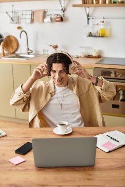 Yakışıklı genç profesyonel ahşap bir masada oturuyor, gülümsüyor ve kulaklıkla müzik dinliyor..