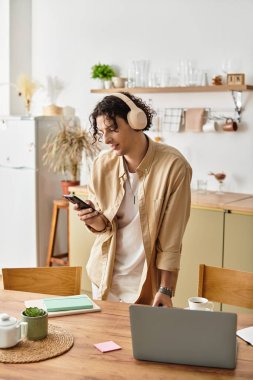 Gündelik giysiler içinde yakışıklı bir genç adam müzik dinler ve rahat bir çalışma alanında telefonunu kontrol eder..