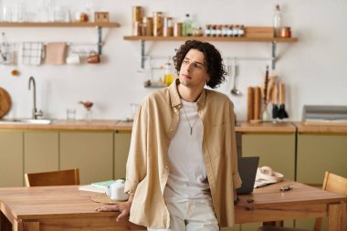 Sıradan iş kıyafetleri içindeki yakışıklı genç adam minimalist bir çalışma alanında düşünceli bir şekilde duruyor..