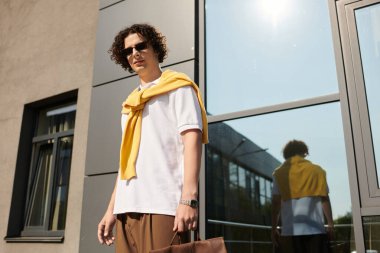 Modern bir binanın dışında şık bir genç adam poz veriyor, zarafet ve güven yayıyor..