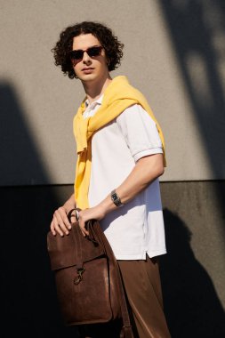 Genç adam, şehirde bir çanta tutarken modern bir iş görüntüsü sergiliyor..