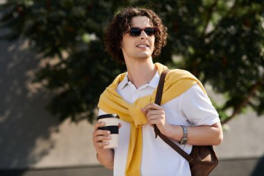 İş elbiseleri içindeki yakışıklı genç adam kahve ile yürüyor, kendine güveni ve tarzı var..