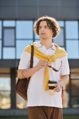 Şık iş dünyasındaki yakışıklı genç adam açık gökyüzünün altında gezinirken kahvesini yudumluyor..