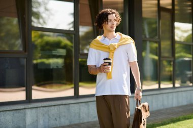 Genç bir adam elinde kahve fincanı ve çantasıyla rahatça yürür ve tarzıyla hava atar..
