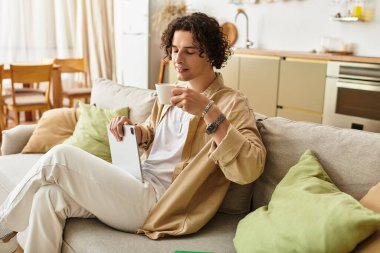 Yakışıklı genç adam kanepede dinleniyor, şık bir ortamda tablet kullanırken kahvesini yudumluyor..