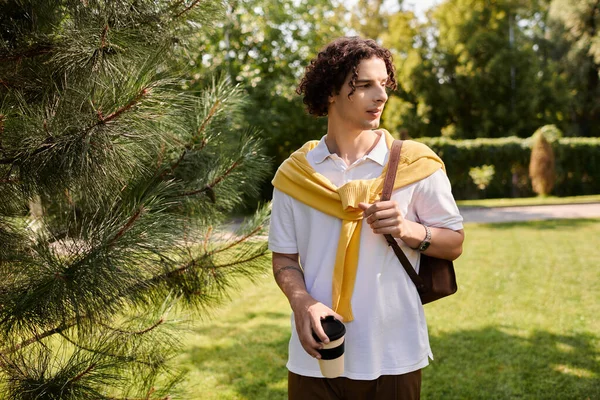 İş kıyafeti giymiş yakışıklı genç adam yemyeşil bir ortamda kahve ile geziniyor..