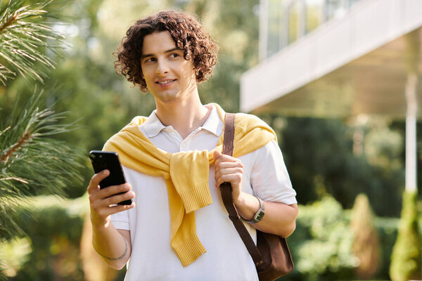 Handsome young man in business attire stands in greenery, phone in hand, exuding confidence.