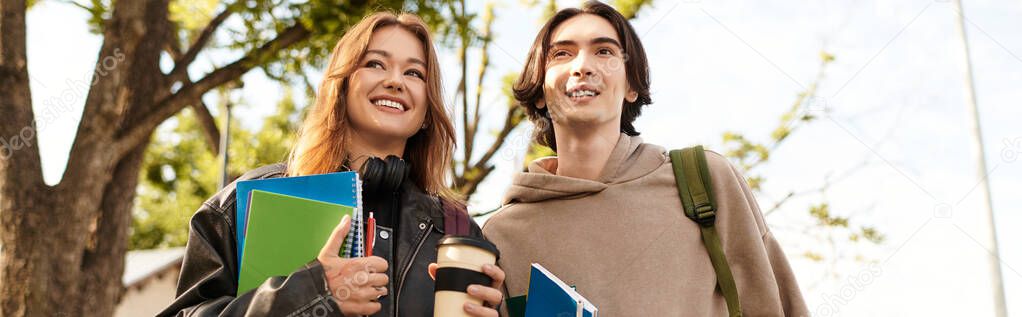 A young couple walks happily through a sunny park, sharing laughter and holding notebooks.