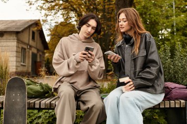 Açık havada sakin bir yerde, genç bir çift telefonlarına bakarken gülümsüyor..