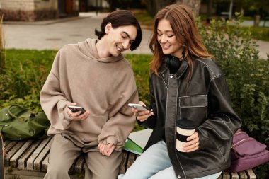 İki genç aşık dışarıda neşeli bir anı paylaşıyor, park ortamında telefonlarına bakıyorlar..