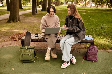 Genç bir çift, güzel yeşil bir park ortamında bir bankta dinlenirken dizüstü bilgisayarda iş birliği yapıyor..