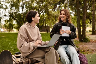 İki genç dışarıda birlikte oturup, elinde dizüstü bilgisayarla mutlu bir şekilde ders çalışıyorlar..