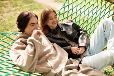 Genç bir çift hamakta dinleniyor, güneşli bir park ortamında kahkahalarını ve sıcaklığını paylaşıyor..