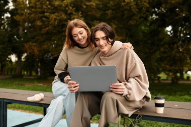 Sevgi dolu bir çift, güzel bir açık hava ortamında dizüstü bilgisayarla çalışırken gülümseyerek yan yana oturur..