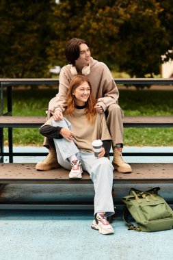 Genç bir çift, doğa ve neşe ile çevrili bir bankta otururken sıcak bir kucaklaşmayı paylaşır..