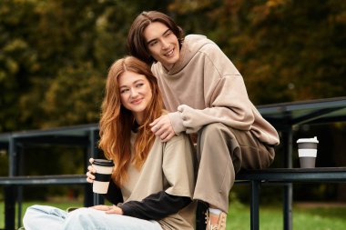 Sevgi dolu çift açık hava parkında oturur, kahveyi yudumlarken gülümsemelerini ve sıcaklığını paylaşırlar..