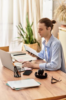 Genç yakışıklı bir adam ahşap bir masada oturuyor, dizüstü bilgisayarına odaklanmış ve rahat bir evde notlar alıyor..