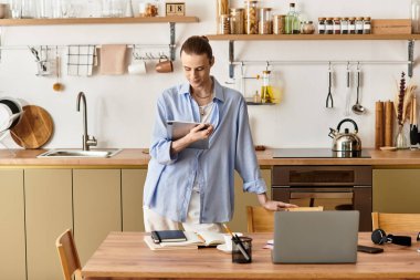 Genç bir adam şık bir mutfakta rahatça durup tabletine odaklanıyor..