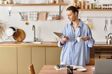 Dişi genç adam, modern bir mutfakta kahve ve notlarla, sakin bir sabahı kucaklıyor..