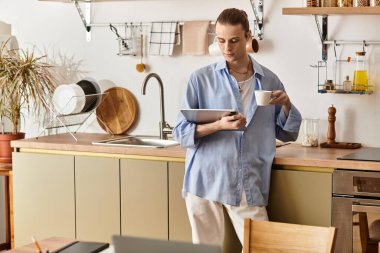 Zarif genç adam şık bir mutfakta duruyor, içkisini yudumluyor ve rahatça tablet kullanıyor..