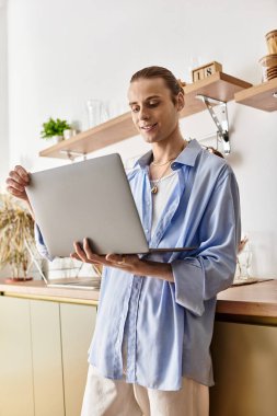 Genç, çekici bir adam şık bir mutfakta dizüstü bilgisayarına odaklanmış ve gülümsüyor..